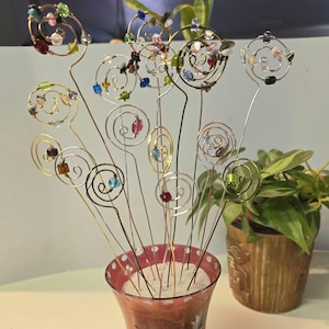 May include: A bouquet of wire and bead floral stems in a red and white polka dot vase. The stems are made of wire and have small, colorful beads attached to them. The beads are arranged in a spiral pattern on the stems. The vase is filled with sand.