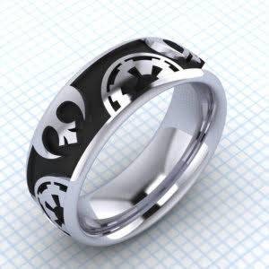 May include: A silver ring with a black band featuring a repeating pattern of a stylized symbol. The ring has a polished finish and a rounded profile. The design is a mix of geometric and abstract shapes.