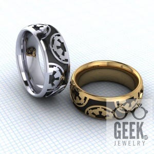 May include: Two wedding bands with a black and gold design. The bands feature a repeating pattern of the Imperial symbol from Star Wars.