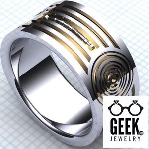 May include: A silver-toned ring with gold accents and a detailed design. The ring features a stylized lightsaber and a spiral pattern. The Geek Jewelry logo is visible in the lower right corner.