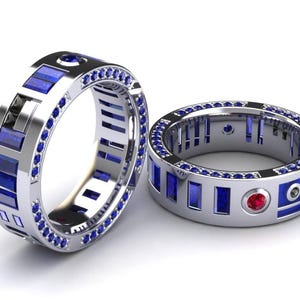 May include: Two silver rings with blue and red gemstone accents. One ring features a series of blue rectangular stones and a row of smaller blue stones. The other ring has a similar design with a red gemstone.