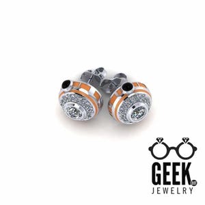 May include: A pair of silver stud earrings with an orange and white design, encrusted with small clear crystals. The earrings have a central, larger clear crystal. The earrings are set against a white background. The Geek Jewelry logo is in the bottom right corner.