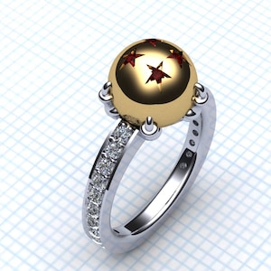 May include: A gold ring featuring a round, yellow and red gemstone set in the centre. The gemstone has five red stars on it. The ring band is silver and has small, clear gemstones set around it.