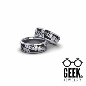 May include: Two silver wedding bands with a black enamel design featuring a repeating pattern of a building with a phone booth on top. The bands are stacked on top of each other.