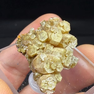 May include: A cluster of pale yellow, hexagonal prismatic crystals with a fibrous, slightly metallic luster. The mineral specimen features tightly packed, vertically striated columns that form a dense, irregular formation with a light tan hue.
