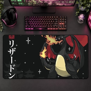 May include: A black rectangular desk mat featuring a graphic of a black dragon with red wings breathing fire. The design includes white Japanese katakana text reading リザードン, a red square with a kanji character, and white star accents on a dark background.
