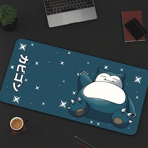 May include: A blue and white cartoon character, Snorlax, is sleeping on a blue mouse mat with white stars. The mouse mat has the Japanese word "Snorlax" written on it in white.