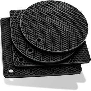 Può includere: Tre sottopentola in silicone nero con un motivo a nido d'ape. Il sottopentola più grande è rotondo, e i due più piccoli sono quadrati.