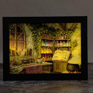 Könnte beinhalten: Ein rechteckiger Schattenkasten mit einem beleuchteten Diorama eines Apotheken-Interieurs. Die Szene zeigt Regale voller bunter Glasflaschen, ein großes aufgeschlagenes Buch, einen dampfenden schwarzen Kessel und einen Holztisch mit Kräutern.