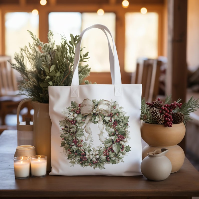May include: A white tote bag featuring a watercolor wreath design with holly, berries, and a bow. The bag has a simple handle design and is displayed on a wooden table. The scene includes candles, vases, and greenery, creating a festive atmosphere.