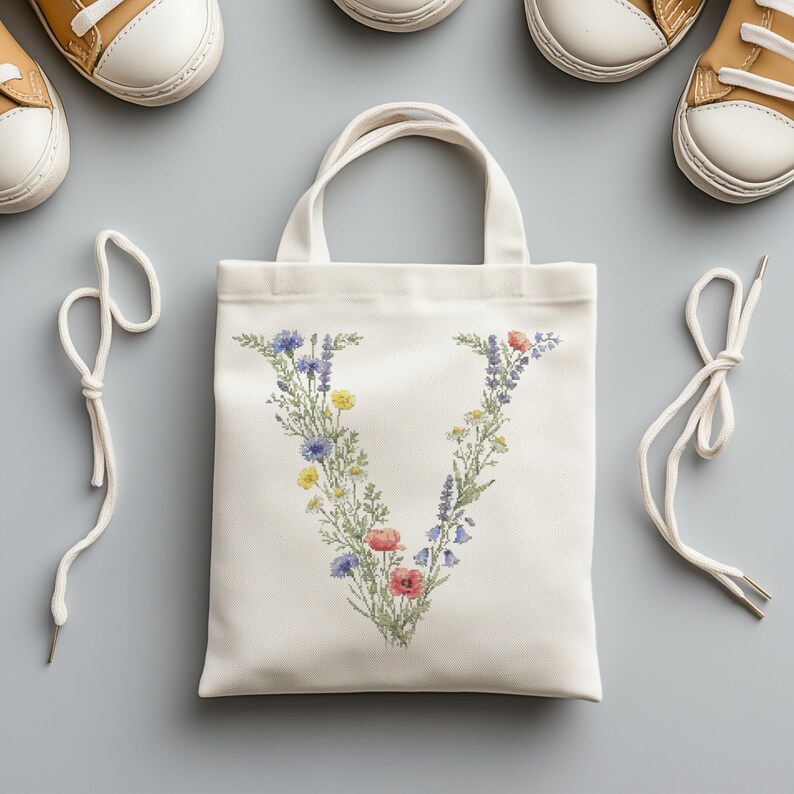 May include: A white canvas tote bag with a floral "V" design in blue, yellow, and red. The bag has two handles and is surrounded by white shoelaces and two pairs of tan and white sneakers.