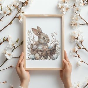 Könnte beinhalten: Ein braunes Kaninchen sitzt in einem geflochtenen Korb, der mit bunten Ostereiern gefüllt ist. Der Korb ist von zarten weißen Blumen und grünem Laub umgeben.