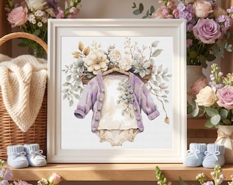 Op de afbeelding: Een ingelijst kruissteekontwerp met een baby-outfit: een lavendelkleurig vest, een witte romper en bijpassende bloomers. Het ontwerp is versierd met bloemmotieven. De afbeelding staat op een houten plank, met babyschoentjes en een mand op de achtergrond.