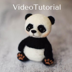 Peut inclure: Un petit ours en peluche panda fait à la main en feutre noir et blanc. Le panda a un nez noir et de petits yeux noirs. Le panda est assis sur une surface gris clair.