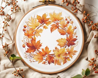 May include: A cross-stitch embroidery hoop with a wreath of autumn leaves in shades of orange, yellow, and red. The leaves are arranged in a circular pattern, creating a festive and seasonal design.