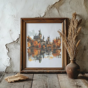 May include: A framed watercolor painting of a castle with a reflection in the water. The castle is surrounded by trees with orange and yellow leaves. The painting is in a brown wooden frame.