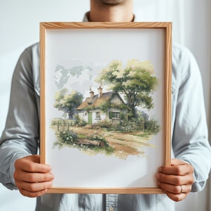 May include: A framed cross-stitch embroidery depicting a quaint cottage with a thatched roof, surrounded by lush greenery and a dirt path leading to the front door.