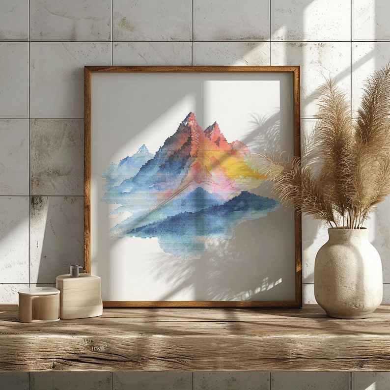 May include: A framed watercolor painting of a mountain range with a blue, pink, and yellow color scheme. The mountains are depicted in a stylized, pixelated style.