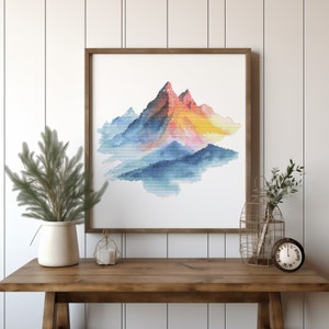 May include: A framed watercolor painting of a mountain range with a blue, pink, and yellow color scheme. The mountains are surrounded by a light blue haze.