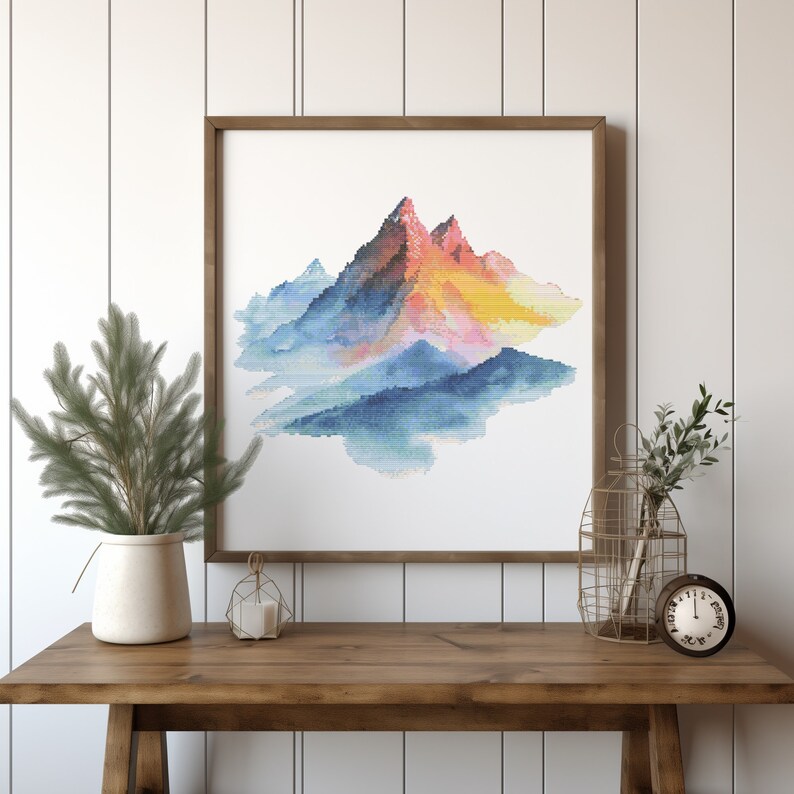 May include: A framed watercolor painting of a mountain range with a blue, pink, and yellow color scheme. The mountains are surrounded by a light blue haze.