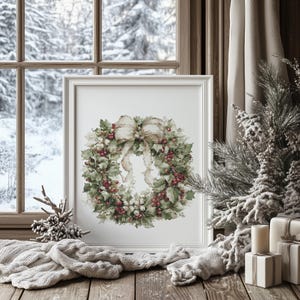 May include: A framed watercolor print of a Christmas wreath with red berries, green leaves, and a cream-colored bow. The print is displayed on a wooden surface with a snowy winter scene visible through a window in the background.