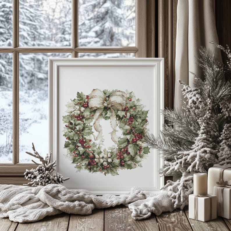 May include: A framed watercolor print of a Christmas wreath with red berries, green leaves, and a cream-colored bow. The print is displayed on a wooden surface with a snowy winter scene visible through a window in the background.