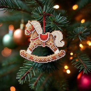 May include: A handcrafted Christmas ornament shaped like a rocking horse, made with a cross-stitch design. The ornament features a cream-colored mane and tail, with a red saddle and accents. It hangs from a red string on a Christmas tree.