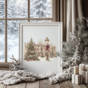 Könnte beinhalten: Ein gerahmter Druck zeigt eine winterliche Szene mit schneebedeckten Häusern und einer Straßenlaterne mit roter Schleife. Ein Weihnachtsbaum ist zu sehen. Der Druck ist vor einem verschneiten Fenster platziert, mit Schal und Tannenzweigen.
