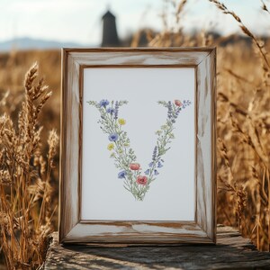 May include: A framed print featuring the letter "V" composed of colorful wildflowers. The flowers include blue cornflowers, yellow blooms, and red poppies. The frame is made of distressed wood, adding a rustic touch to the floral artwork.