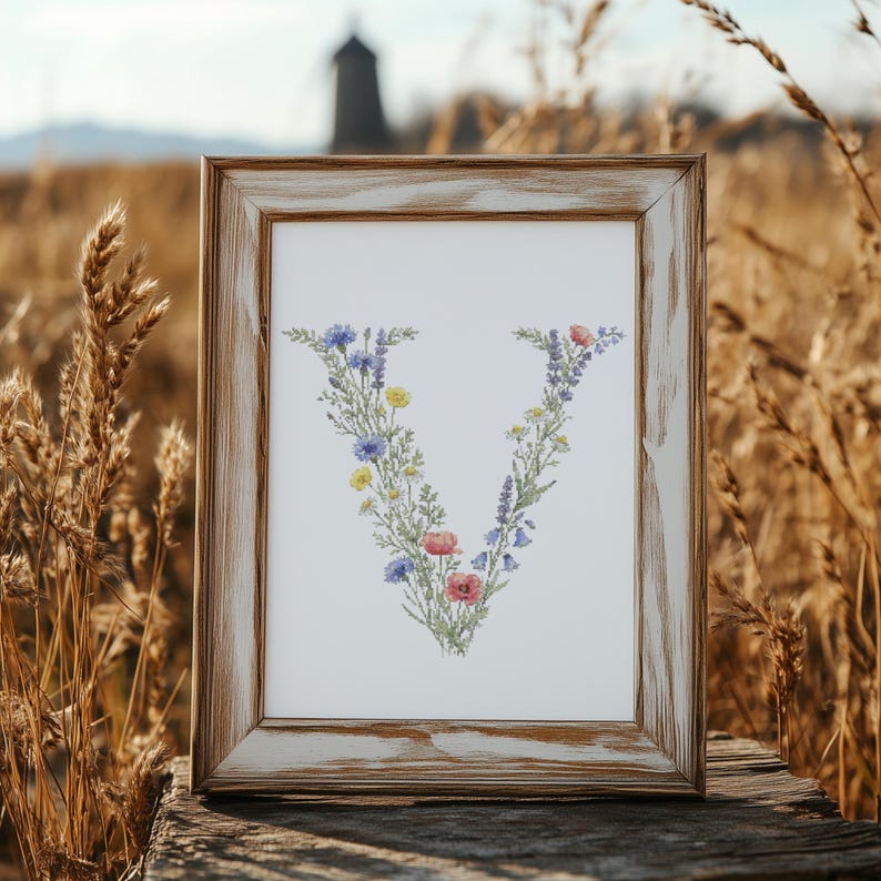 May include: A framed print featuring the letter "V" composed of colorful wildflowers. The flowers include blue cornflowers, yellow blooms, and red poppies. The frame is made of distressed wood, adding a rustic touch to the floral artwork.