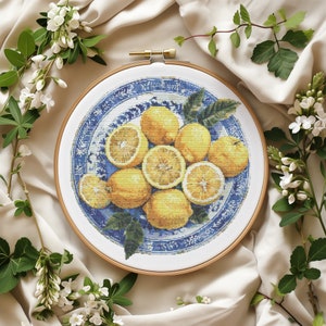 May include: A blue and white porcelain plate with a gold trim border, filled with a still life of lemons. The lemons are arranged in a circular pattern, with some cut in half to reveal their yellow flesh.