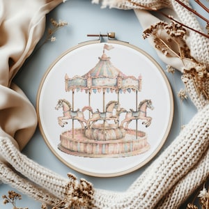 Puede incluir: Un carrusel de estilo vintage con cuatro caballos, pintados en colores pastel suaves, se muestra en un aro de bordado de madera. El carrusel está rodeado de un fondo blanco.