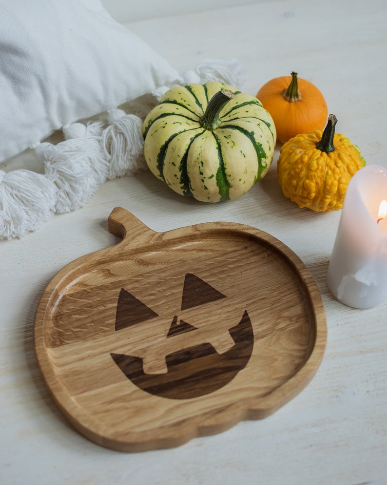 May include: A wooden serving tray shaped like a jack-o'-lantern with a carved face. The tray is surrounded by three small pumpkins, one green and white striped, one orange, and one yellow with bumps.