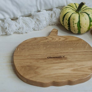 May include: A wooden pumpkin-shaped cutting board with the text "OlewoodLV" engraved on the surface. The board is surrounded by small gourds.