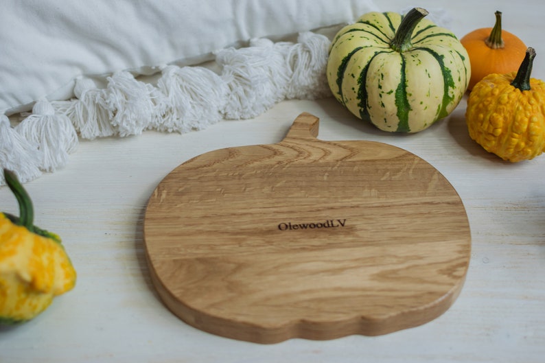 May include: A wooden pumpkin-shaped cutting board with the text "OlewoodLV" engraved on the surface. The board is surrounded by small gourds.