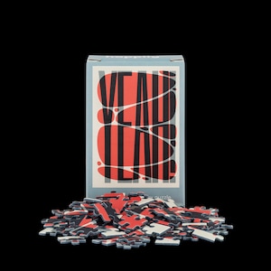 Puede incluir: Una caja de rompecabezas con las palabras "VEAD TEAD" en rojo y negro sobre un fondo azul claro. Un montón de piezas de rompecabezas en rojo, negro y blanco están frente a la caja. Las piezas del rompecabezas están esparcidas sobre un fondo negro.
