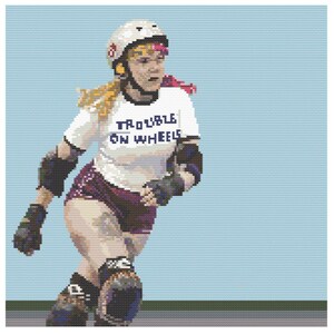 May include: A woman wearing roller skates and protective gear, including a helmet, knee pads, and elbow pads. She is wearing a white t-shirt with the text "Trouble on Wheels" printed on it. She has pink hair and is skating on a blue surface.