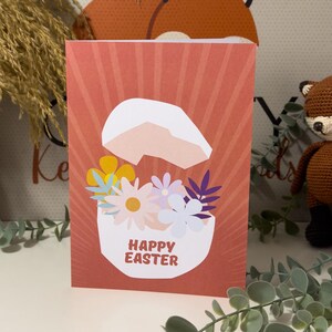 May include: A red and white Easter card featuring a cracked egg with flowers inside. The text "Happy Easter" is written on the egg.