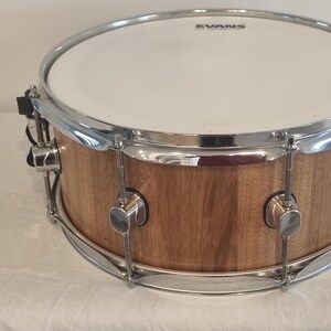May include: A brown wooden snare drum with chrome hardware and an Evans brand drumhead.