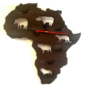 May include: A dark brown wooden clock shaped like the continent of Africa with white silhouette cutouts of animals including an elephant, rhino, lion, buffalo, and zebra. The clock hands are red and black.