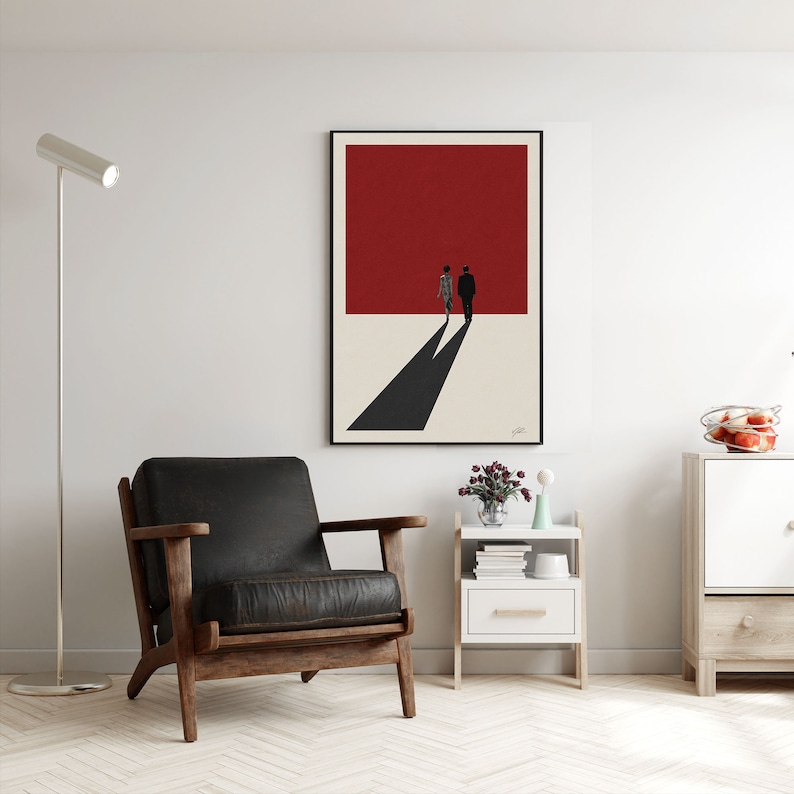 May include: A black and white minimalist art print featuring two figures walking away from a red background. The print is framed in black and hanging on a white wall.