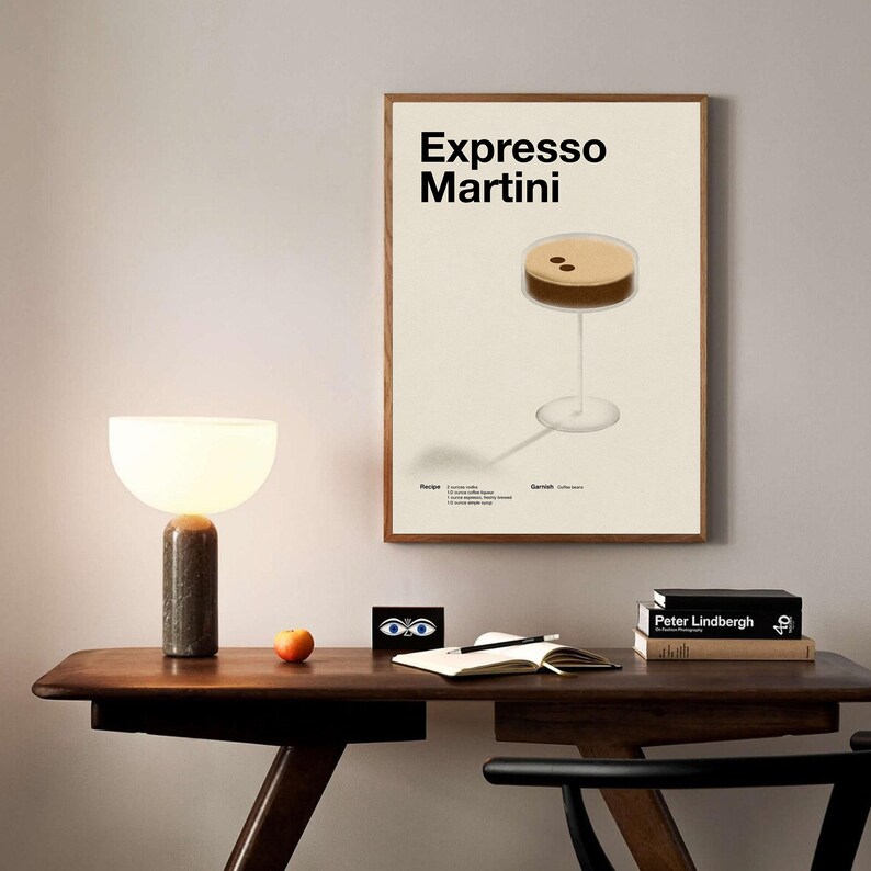 Op de afbeelding: Een minimalistische poster met een witte achtergrond en zwarte tekst die "Espresso Martini" luidt. In het midden van de poster is een bruine en witte illustratie van een espresso martini-cocktail te zien. De poster is ingelijst in een licht houten frame.