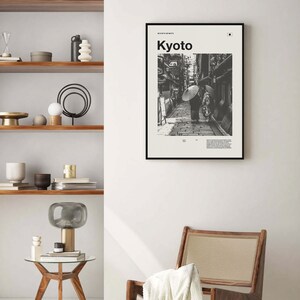 May include: Black and white photograph of a street scene in Kyoto, Japan. Two people walk down a narrow street lined with traditional Japanese buildings. The text "Kyoto" is printed in white on a black background at the top of the image.