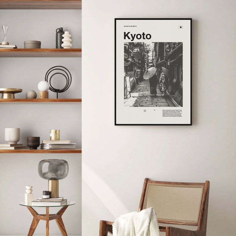 May include: Black and white photograph of a street scene in Kyoto, Japan. Two people walk down a narrow street lined with traditional Japanese buildings. The text "Kyoto" is printed in white on a black background at the top of the image.