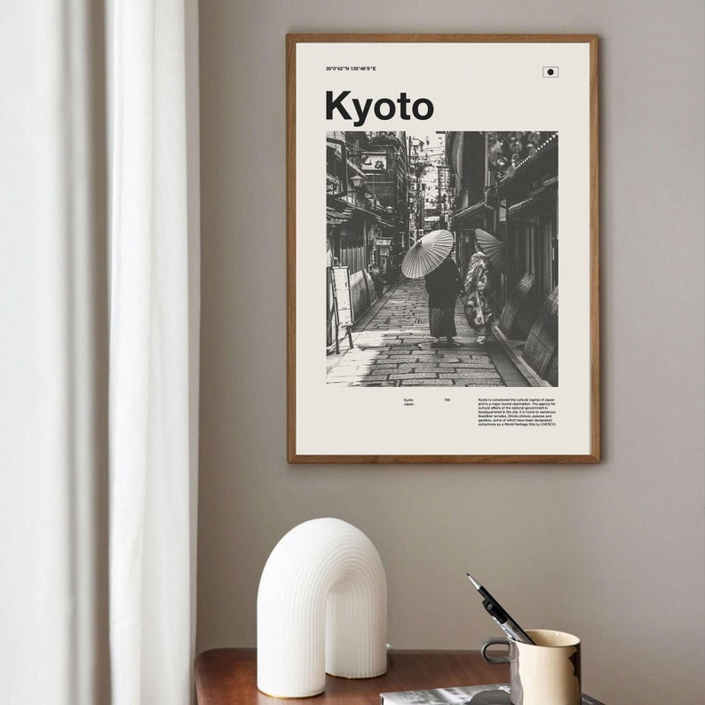 May include: Black and white photograph of a street in Kyoto, Japan. Two people walk down the street, each holding a traditional Japanese umbrella. The text "Kyoto" is printed in bold white letters at the top of the image.