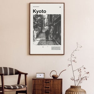 May include: A black and white photograph of a narrow street in Kyoto, Japan. Two people are walking under umbrellas. The image is framed with a white border and the word "Kyoto" is printed in bold black letters at the top.