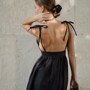 May include: A black sleeveless dress with a low back and tie straps. The dress has a gathered skirt and is made of a lightweight fabric.