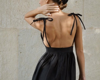 May include: A black sleeveless dress with a low back and tie straps. The dress has a gathered skirt and is made of a lightweight fabric.