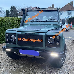 Puede incluir: Un Land Rover Defender 4x4 verde con una parrilla y faros negros. El vehículo tiene un portaequipajes de techo negro y un snorkel negro. El texto "LR Challenge 4x4" está impreso en la parrilla delantera.