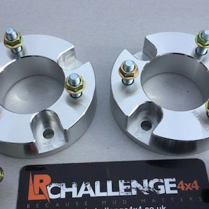 Könnte beinhalten: Zwei silberne Radspacer mit jeweils sechs Schrauben. Die Schrauben haben goldfarbene Muttern. Die Spacer sind mit "56x5.5" gekennzeichnet.